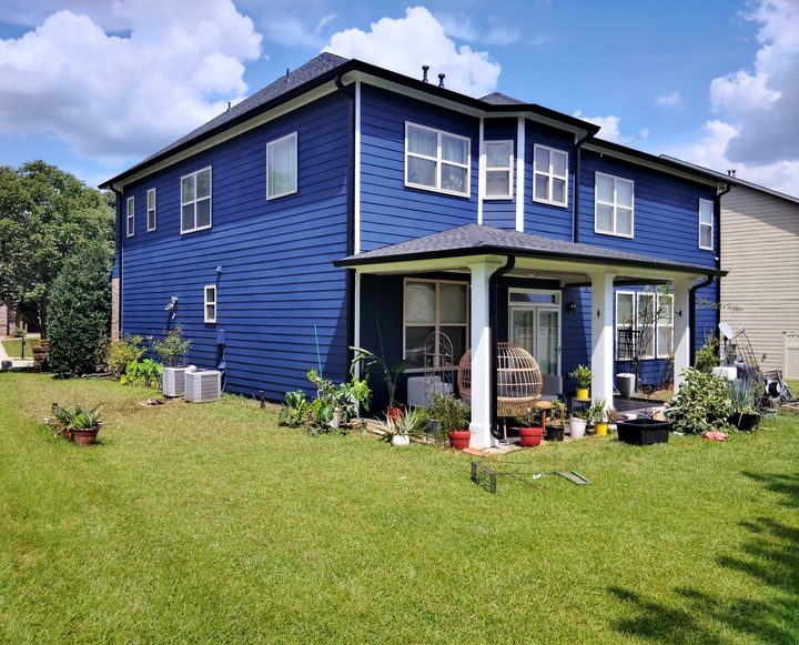Two-story navy home with black gutters and downspouts over a covered patio