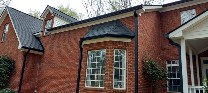 Black gutters and downspouts around the bay window and dormers of a red brick home