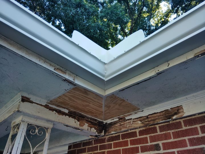 Inside corner of a new white gutter beside freshly replaced soffit wood