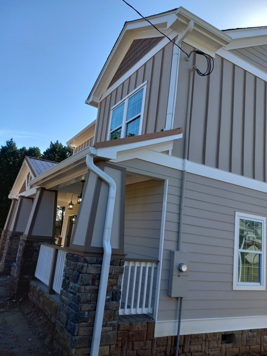 White downspout wrapping a stone porch column on a new craftsman home