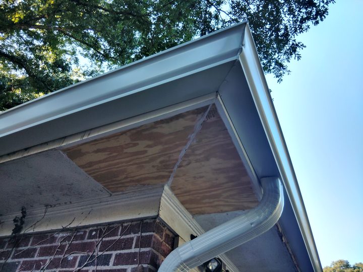 Outside corner with a new white gutter, end cap and downspout elbow on a brick home