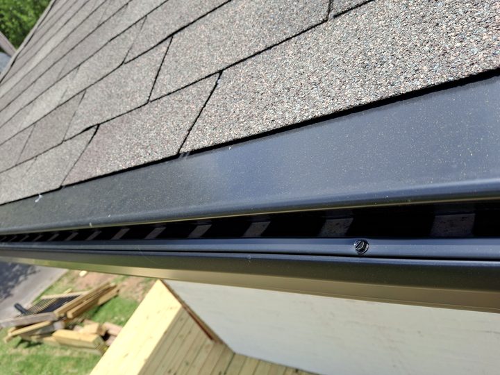 Close-up of a black gutter guard fastened at the shingle edge
